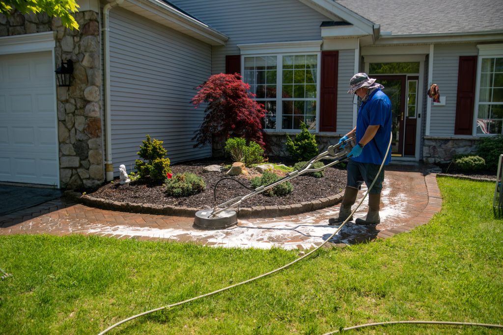 man using a circular power washer to clean a brick walkway in front of a house